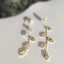 Load image into Gallery viewer, Image shows Diana Dangle Earrings on a white background in direct sunlight with a pair of sunglasses behind them.
