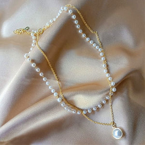 Image shows gold-tone Princess Pearl Necklace laid on pink satin fabric surface.