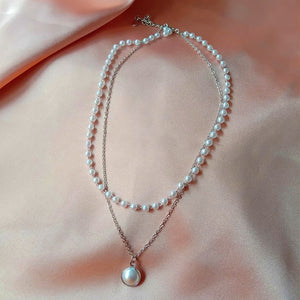 Image shows silver-tone Princess Pearl Necklace laid on pink satin fabric surface.